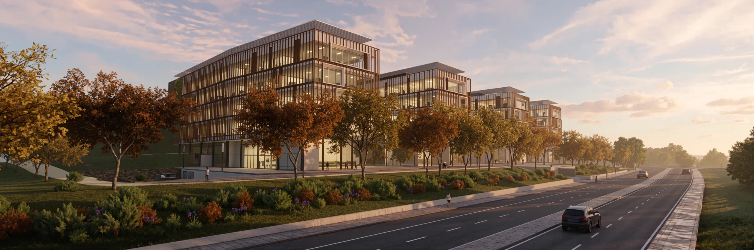 The front of the Loures business park in the late afternoon, with the line of trees along the built edge and the reprofiled EN8 running to the horizon, planted median and cycle lane in place.