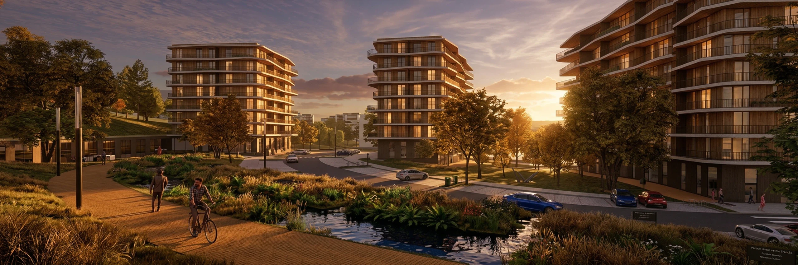 The housing buildings seen from the park in the late afternoon: the timber path with a walker and a cyclist on it, the watercourse and its riparian planting and, beyond to the right, the commercial ground floor along the street.